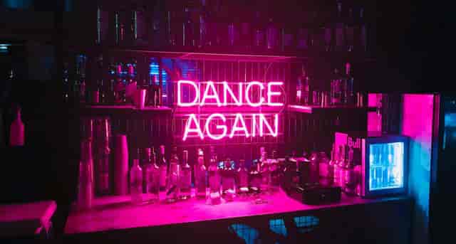 Vibrant bar scene in Stealth with neon "DANCE AGAIN" sign for after-parties and networking.