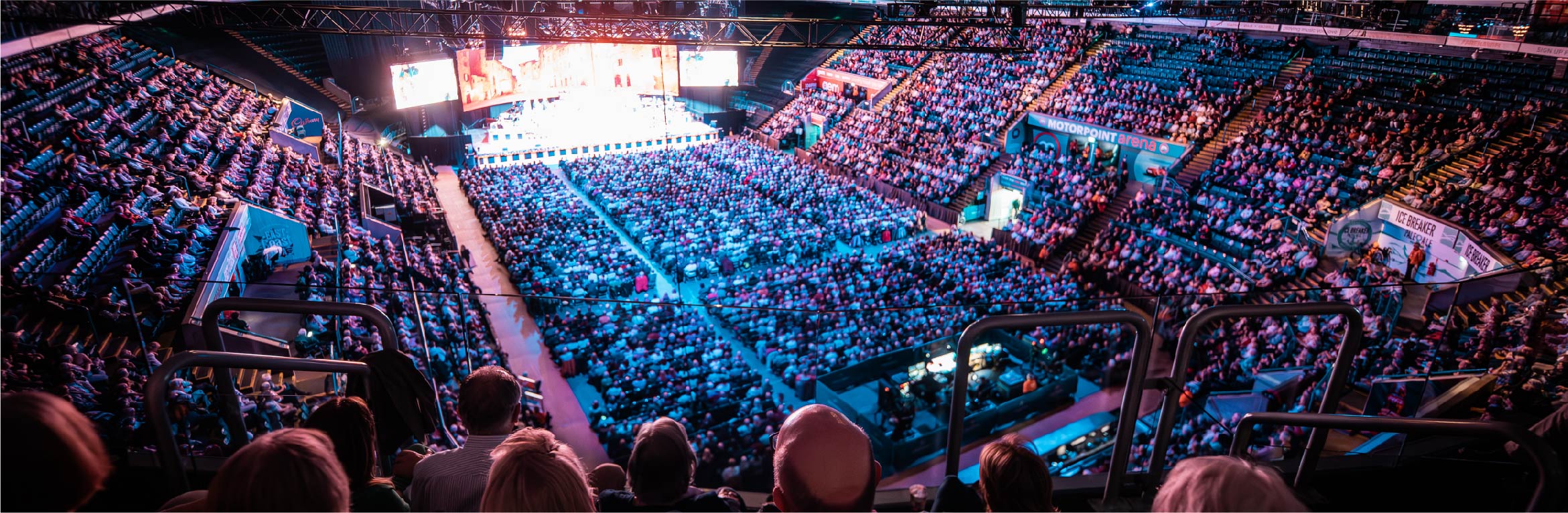 Packed National Ice Centre with dynamic lighting for concert or event.