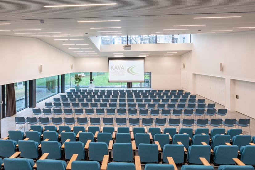 KAVA Congres Centrum auditorium with blue chairs and large screen for conferences and workshops.