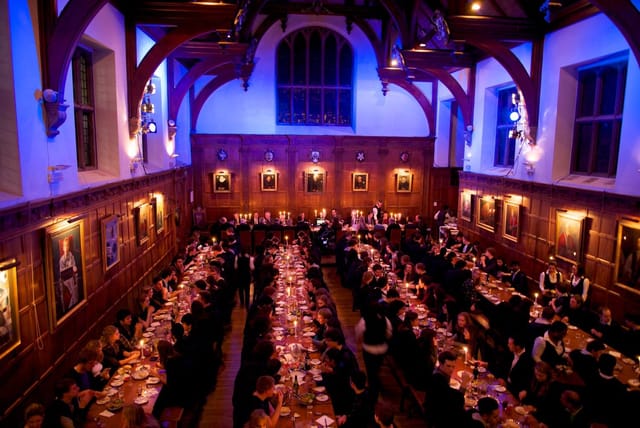 Gala dinner in historic Gonville and Caius College hall with elegant blue uplighting.