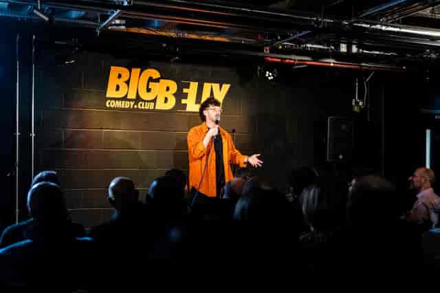Solo comedian on stage at Big Belly Comedy Club, intimate brickwork venue for live stand-up events.