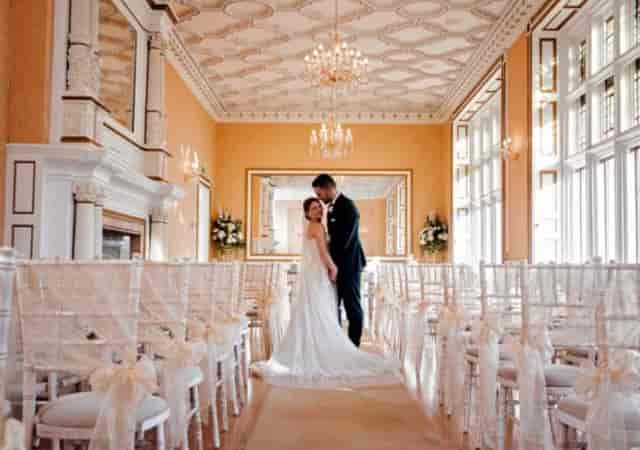 Gold Room wedding ceremony at Holmewood Hall with ornate architecture and elegant Chiavari chairs.