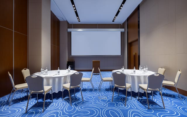 Breakout room at Swissôtel Almaty with banquet tables and projector for corporate meetings.