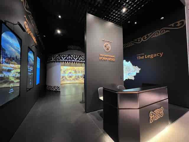 Modern trade show exhibit at QazExpoCongress featuring minimalist desk and digital signage.