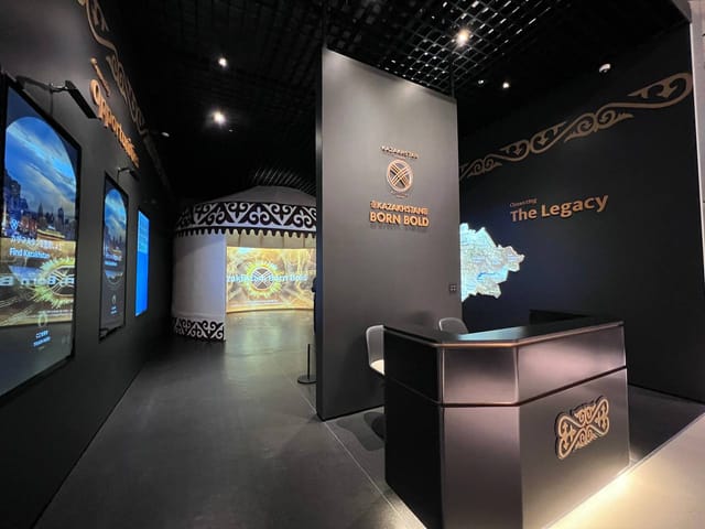 Modern trade show exhibit at QazExpoCongress featuring minimalist desk and digital signage.
