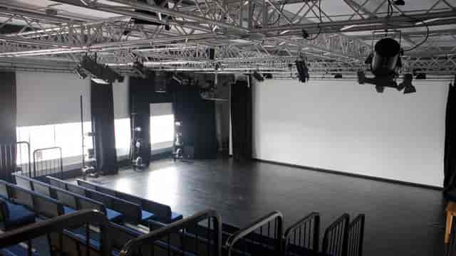 Black-box theatre studio with tiered seating and lighting grid for presentations and workshops.