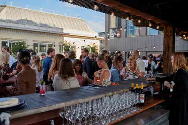 Corporate networking reception on a pavilion terrace with bar and string lighting.