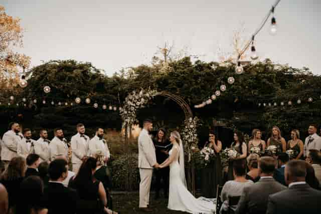 Outdoor wedding ceremony at The New Chichester Hotel with bistro lighting and foliage backdrop.