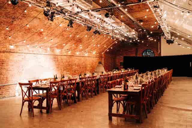 Industrial-chic event venue with brick arches and festoon lighting for corporate galas and banquets.