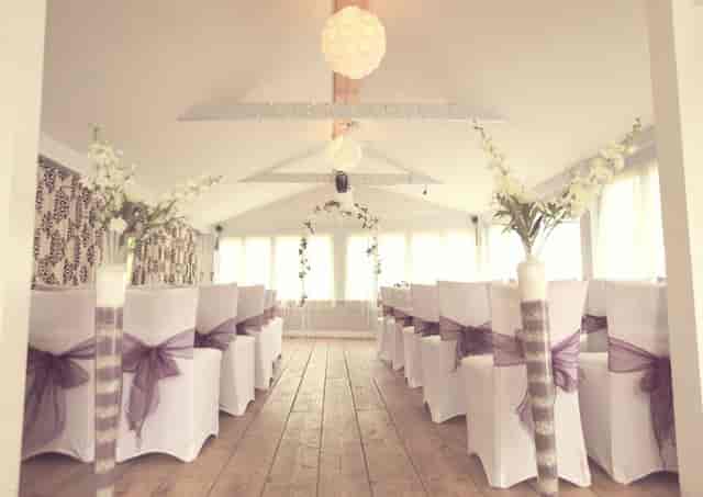 Rustic wedding ceremony setup in Water's Edge function room with white chair covers and floral decor.
