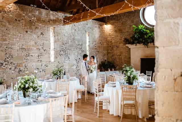 Rustic stone barn wedding reception with round tables and ambient lighting at Fonthill Estate.