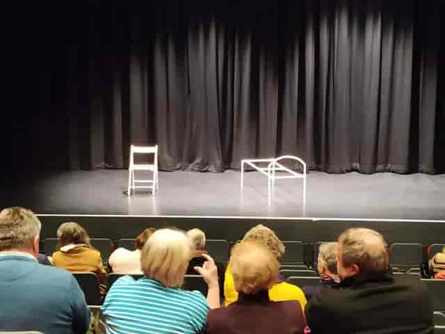 Minimalist stage at The Berry Theatre: chair and table setup for public speaking events.