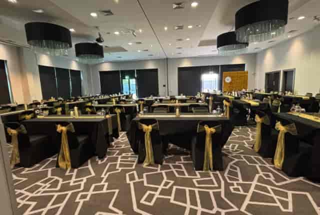 Black and gold banquet hall with long tables for corporate dinners and gala events.
