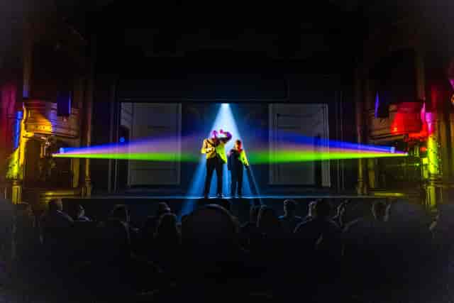 Two presenters on stage with dramatic laser lighting at Bristol Improv Theatre for live events.