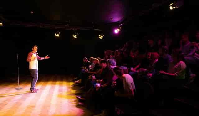 Black-box theater stage with spotlight for stand-up comedy and speaker events.