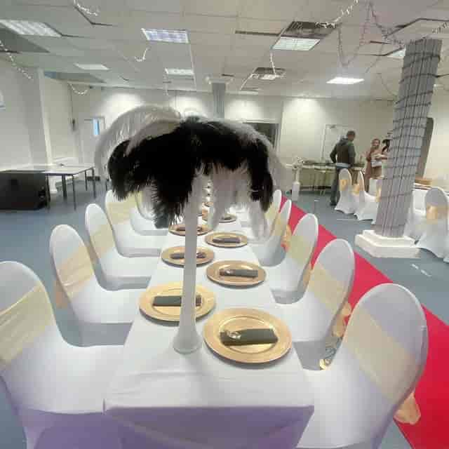 Black-and-white event venue setup with gold chargers and feather centerpieces for gala planning.