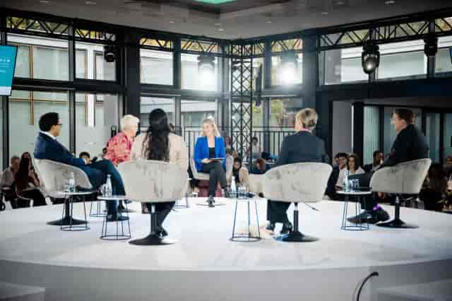 Intimate panel discussion on circular stage in modern glass venue for corporate event networking.
