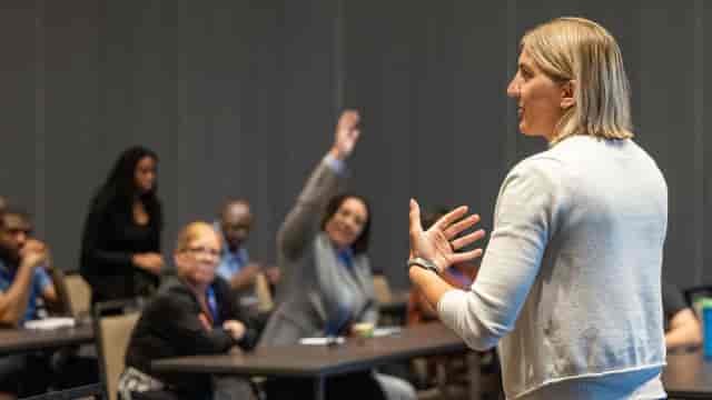 Kings Hall College seminar room with speaker engaging diverse audience during training session.