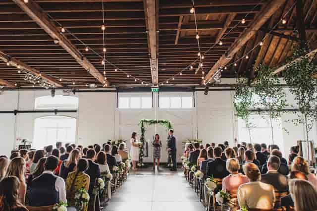 Industrial-chic wedding ceremony at The Chainstore London with floral arbor and string lighting.