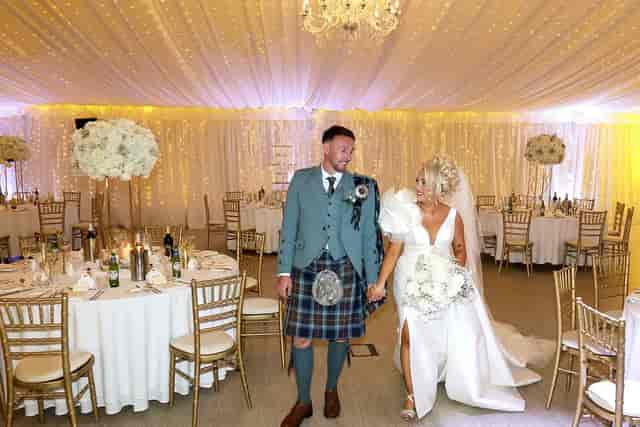 Wedding reception in Grand Marquee with fairy lights, floral centerpieces, and gold Chiavari chairs.