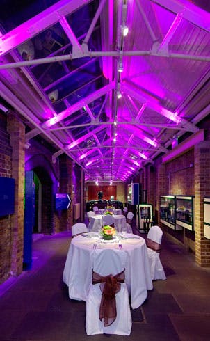 Elegant event space in Tower Bridge with round tables and vibrant purple lighting.