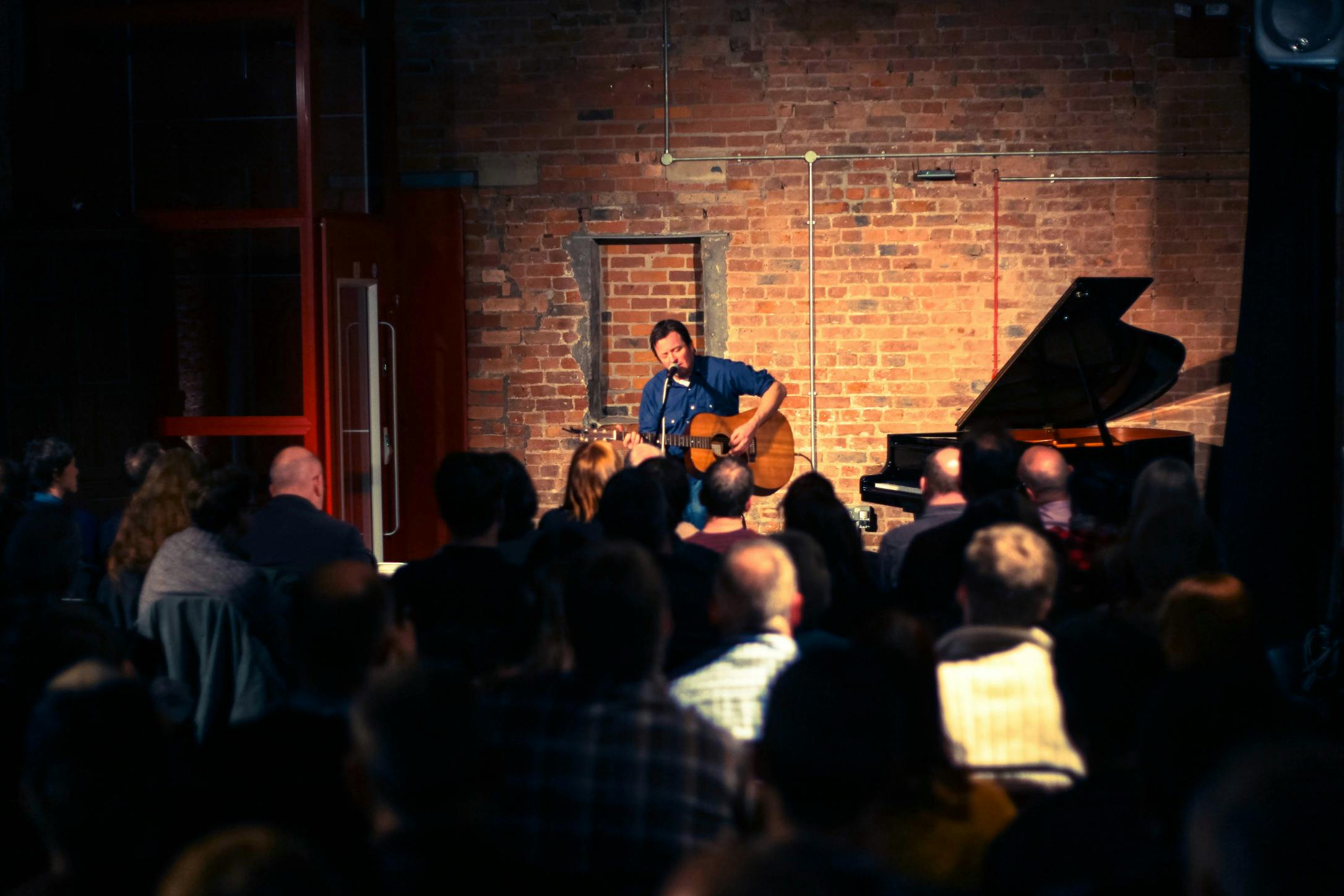 Intimate live performance at The Engine House with warm brick backdrop and engaged audience.