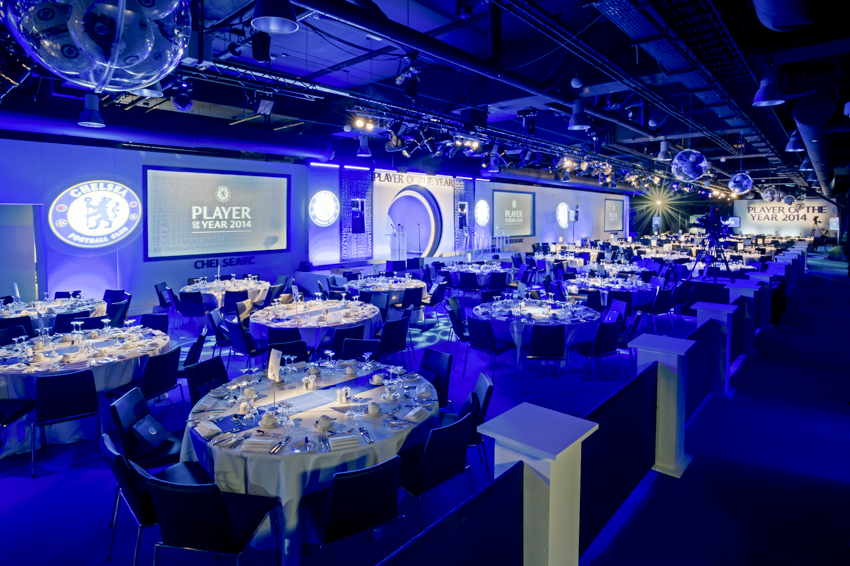 Great Hall at Chelsea FC set for formal dinner, featuring blue tablecloths and ambient lighting. - Banner
