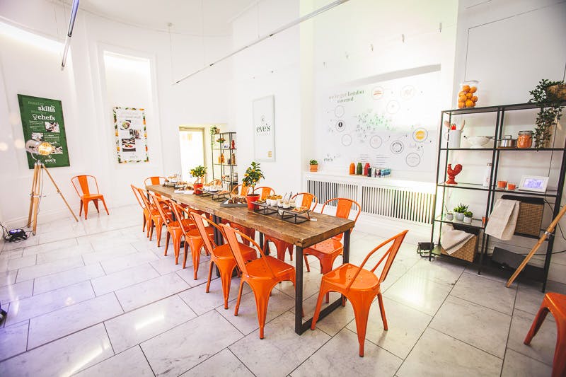 Bright event space with wooden table and orange chairs, ideal for workshops and networking.