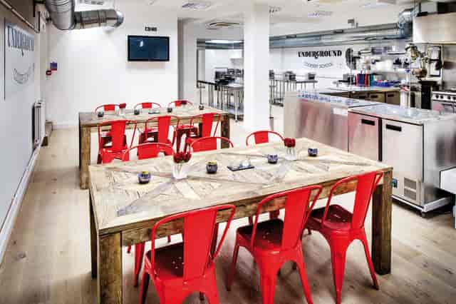 Modern industrial kitchen with large wooden table and red chairs for culinary events.