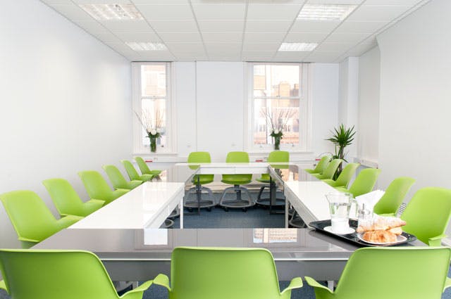 Modern meeting room with U-shaped layout, vibrant green chairs for workshops.