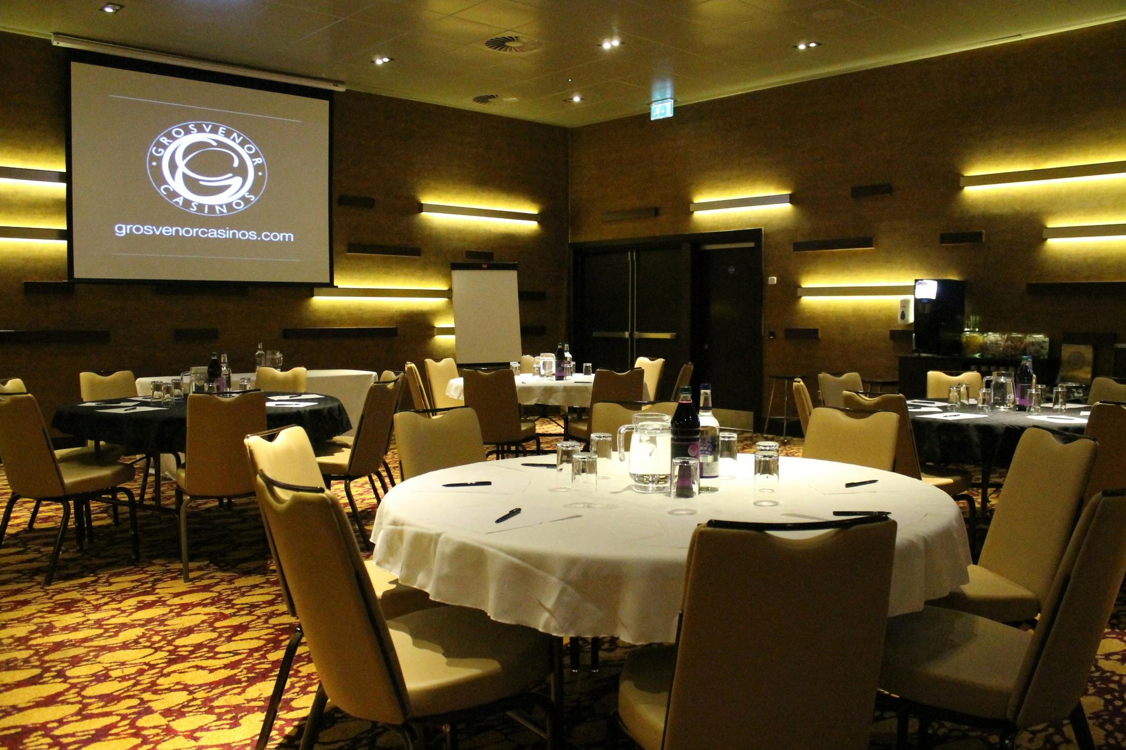 Corporate event setup in Grosvenor Casino Didsbury with round tables and projector.