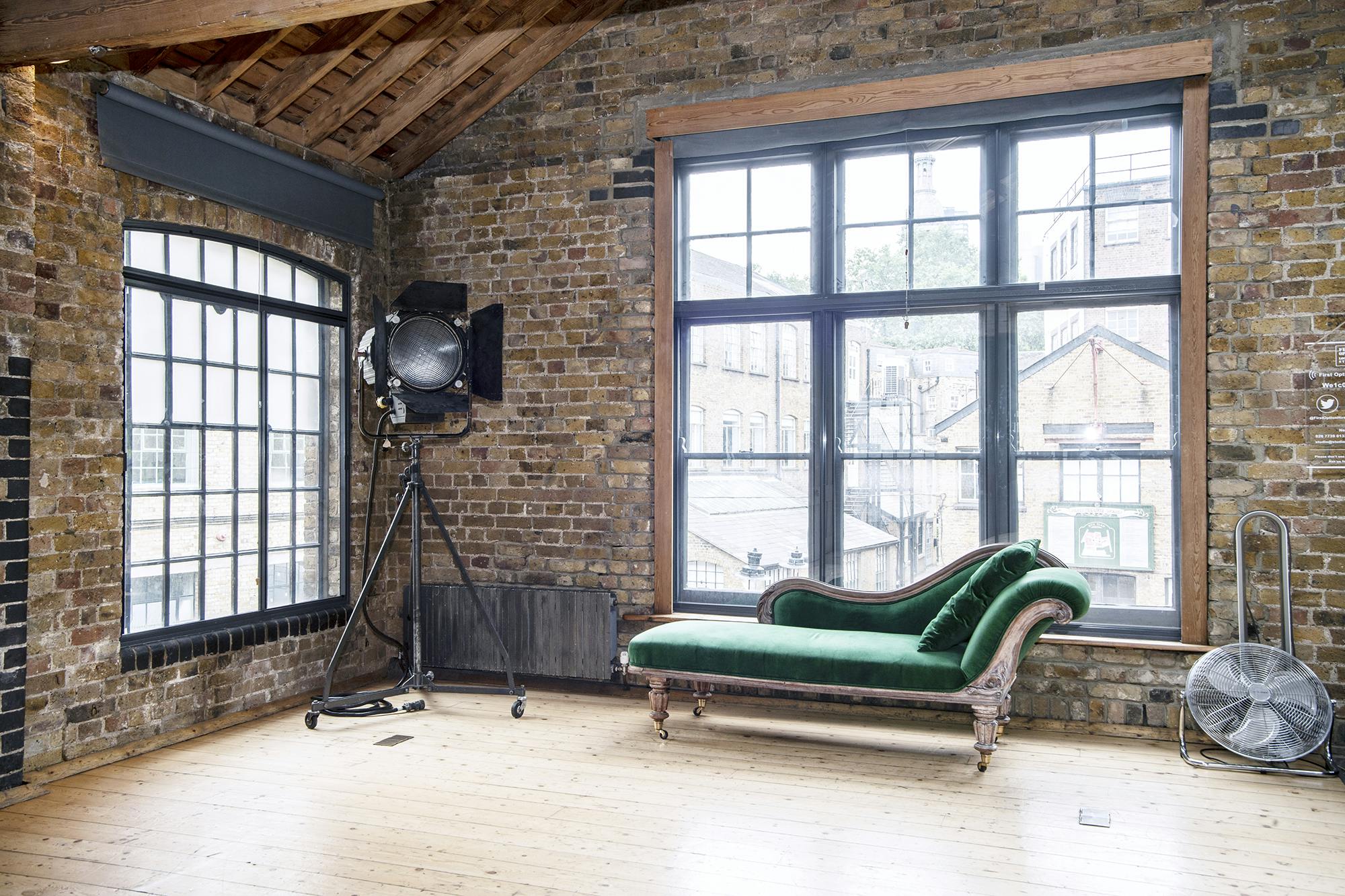 Stylish industrial event space with exposed brick and elegant green chaise lounge.