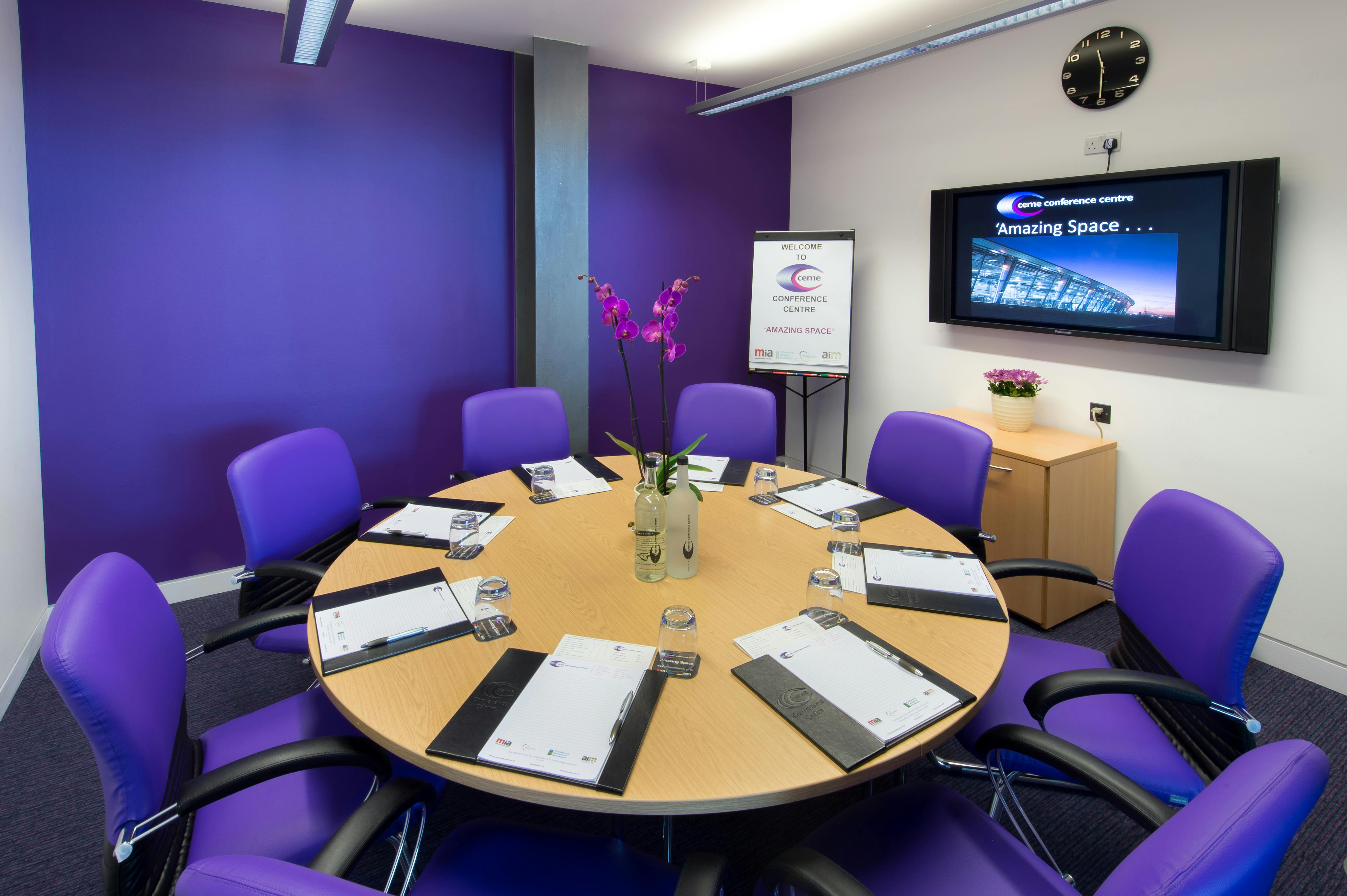 Small meeting room with round table and purple walls for professional events and presentations.