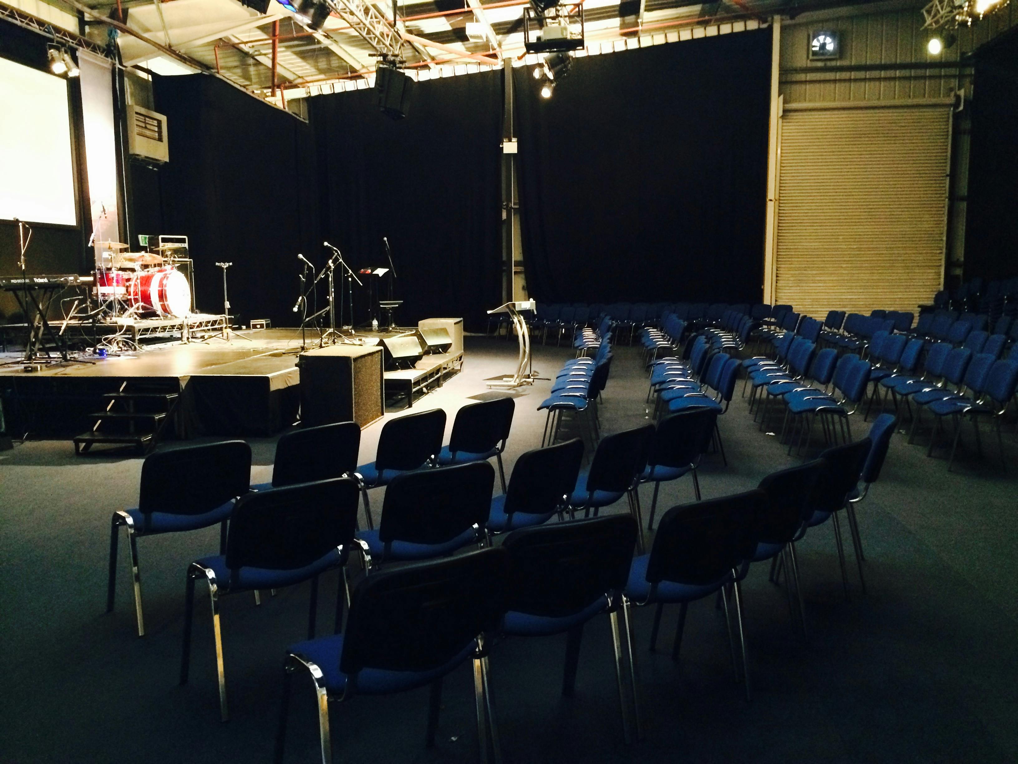 Event space with stage and blue chairs for performances at The Message Enterprise Centre.