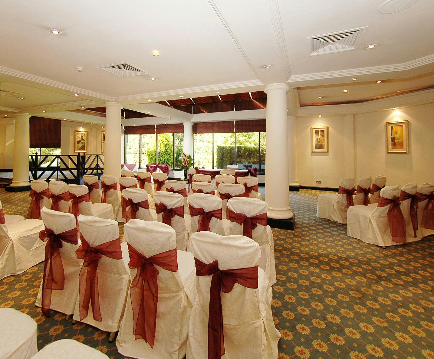 Elegant event space at Portico, Manchester Airport with cream chairs and burgundy sashes.