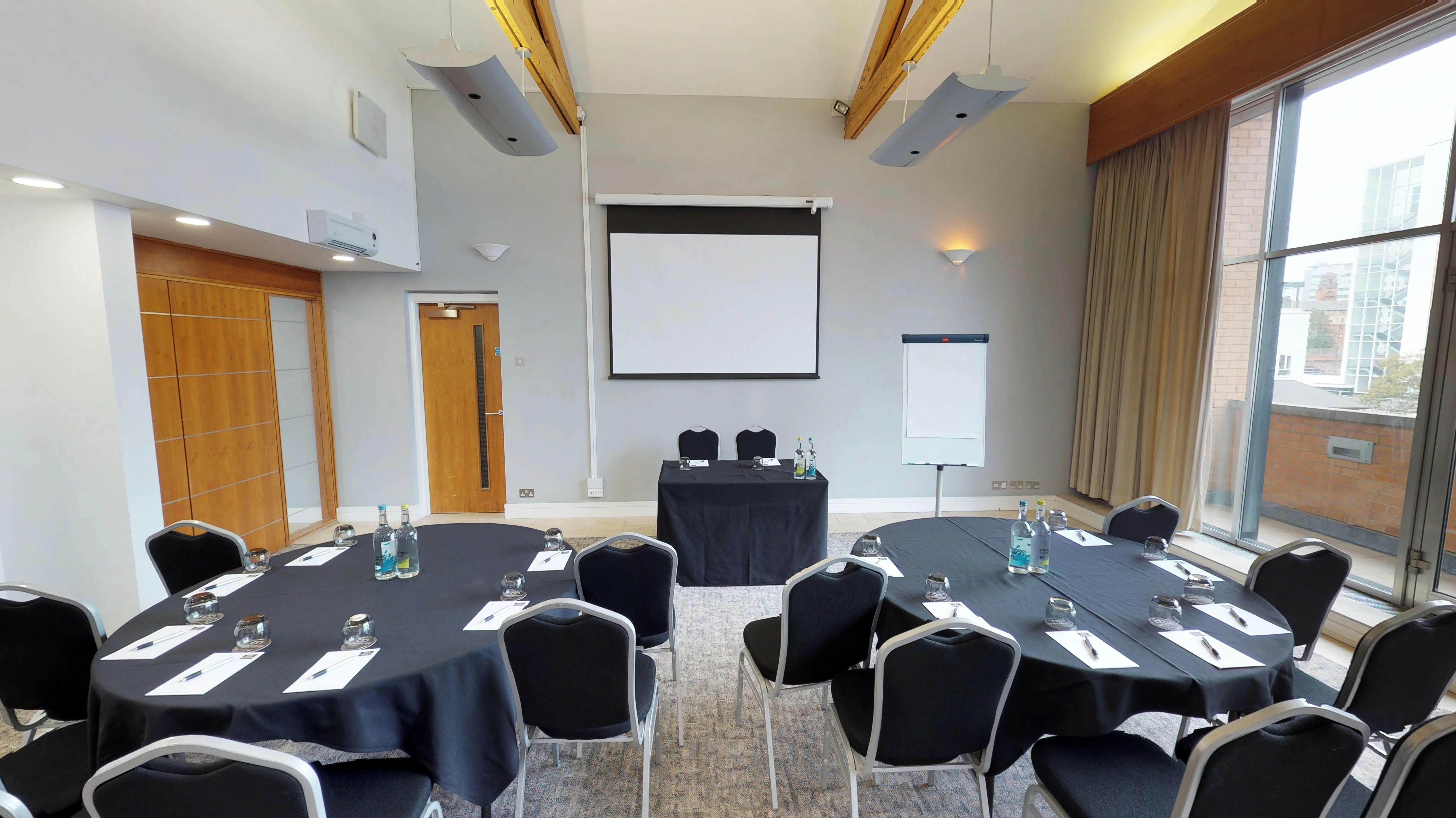 Meeting room with round tables and screen at Manchester Conference Centre for workshops.