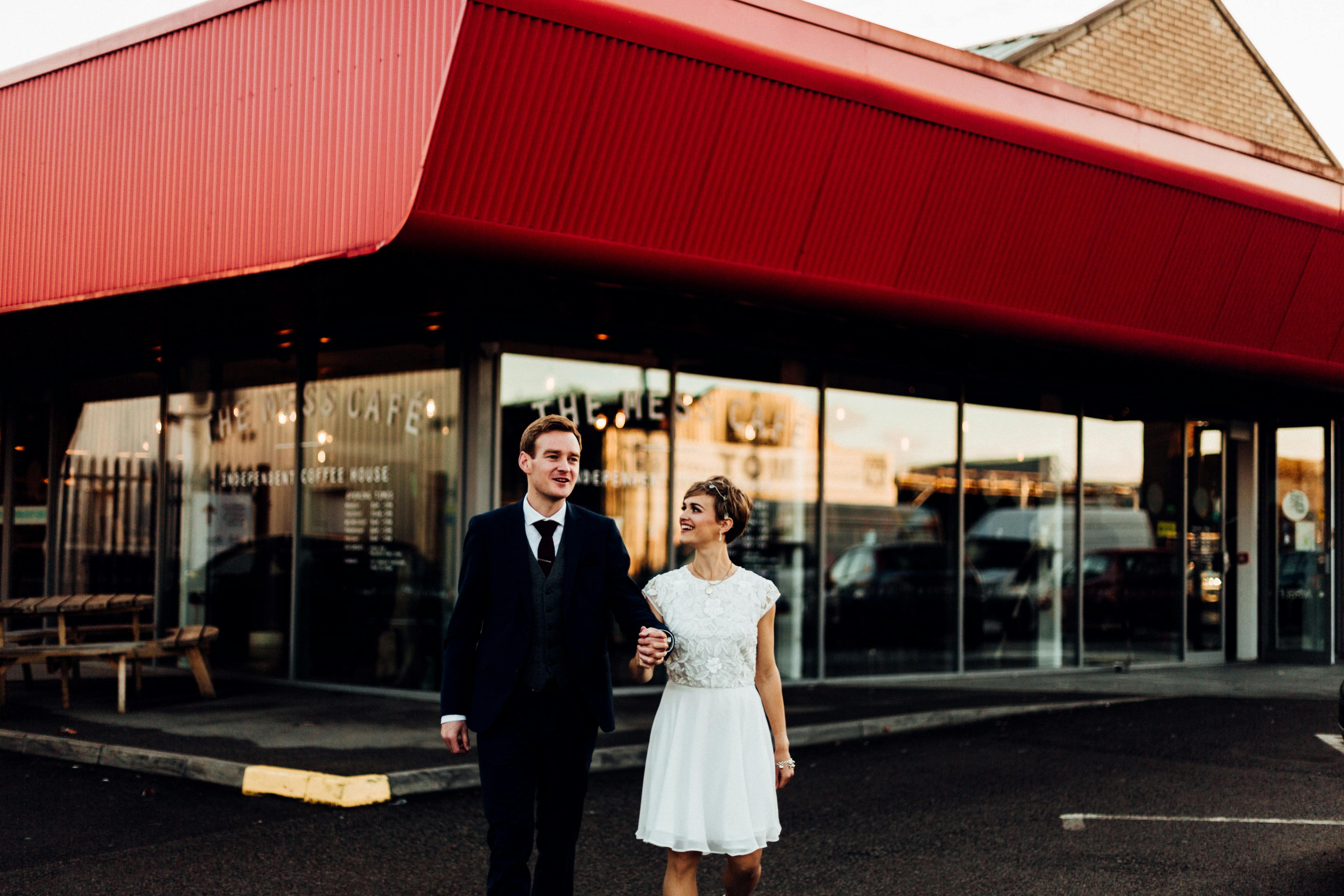 Couple exiting modern venue with red roof, ideal for weddings and celebrations.