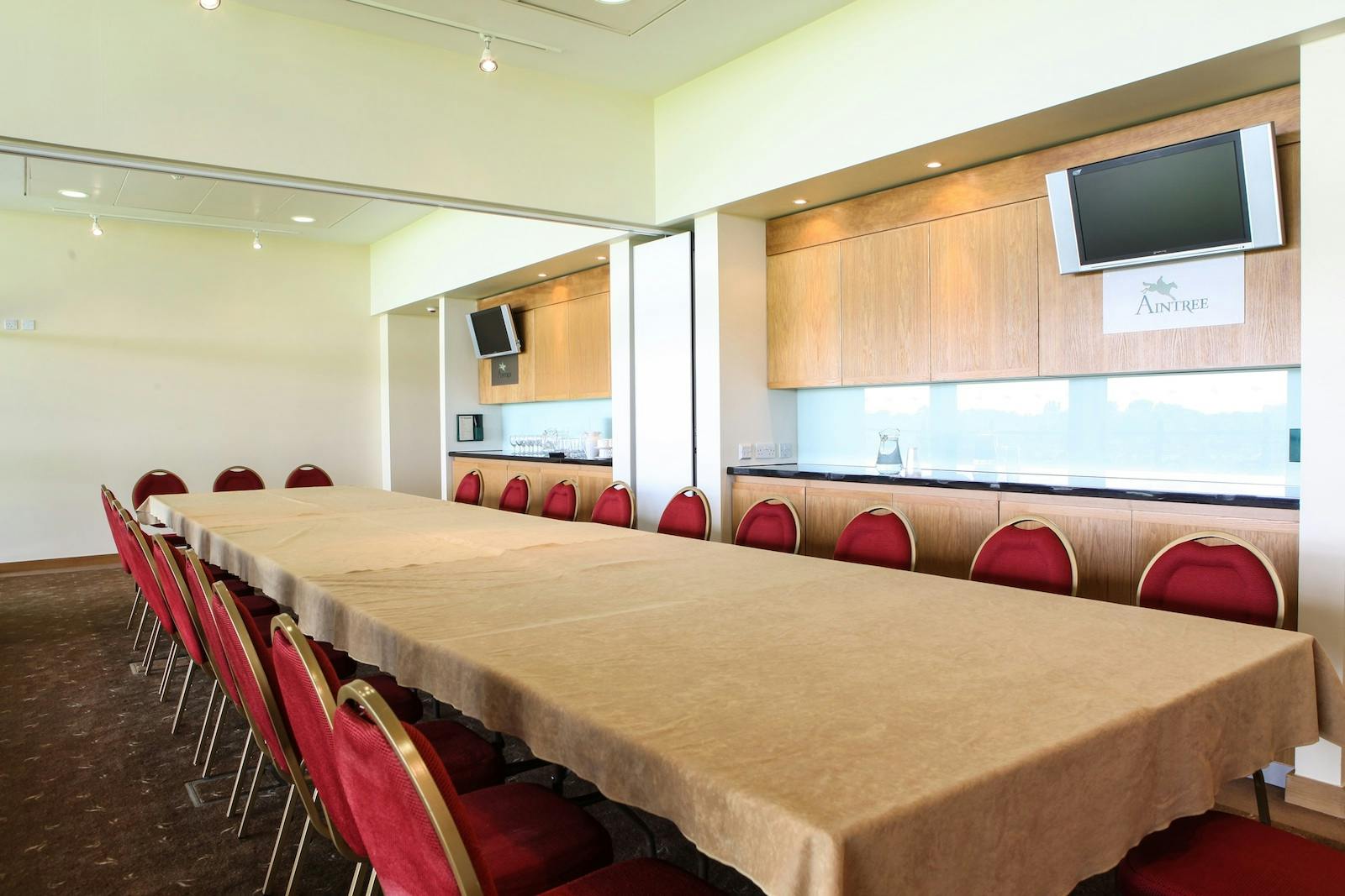 Executive Box at Aintree Racecourse, featuring a long table and red chairs for corporate events.