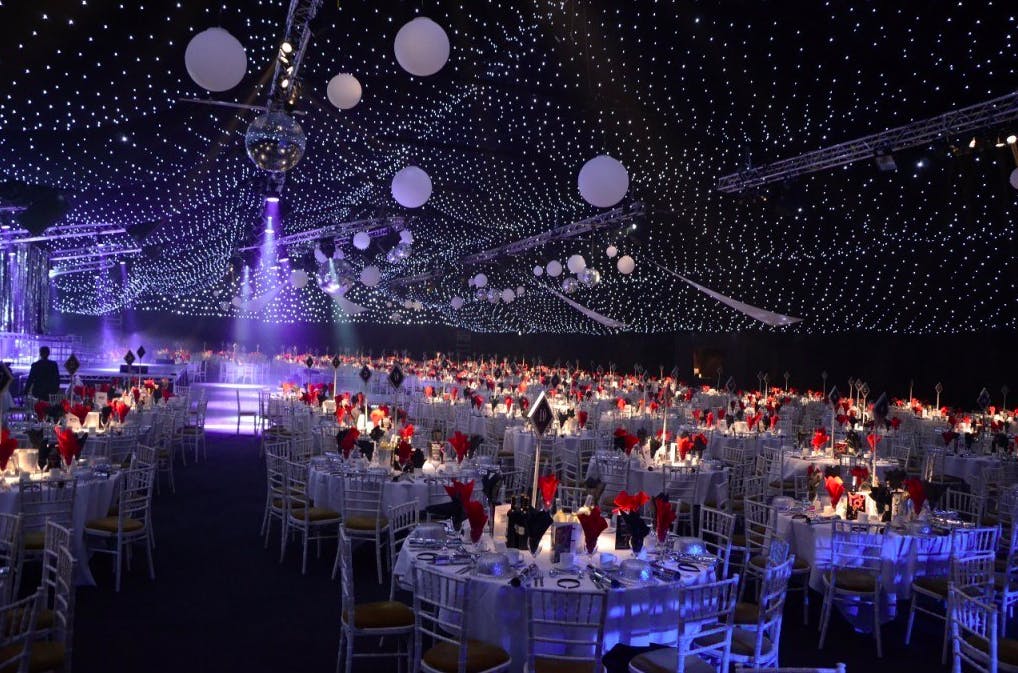 Aintree Racecourse gala with elegant tables and red floral centerpieces under starry canopy.