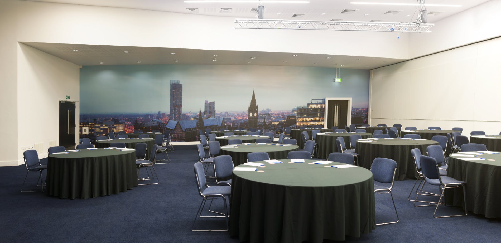 Versatile event space in Manchester with round tables and city skyline backdrop for meetings.