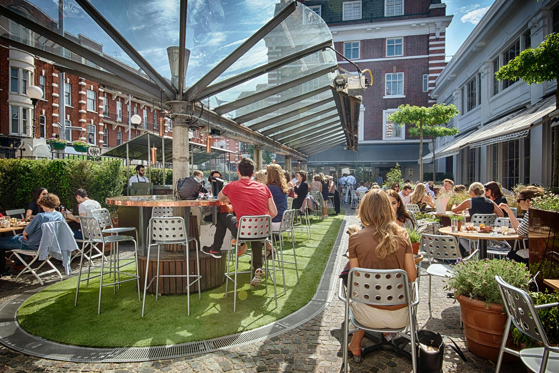 Vibrant outdoor event space at Bluebird Chelsea with communal tables and greenery.