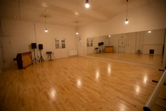 Versatile event space with polished wooden floors and large mirror for workshops and dance classes.