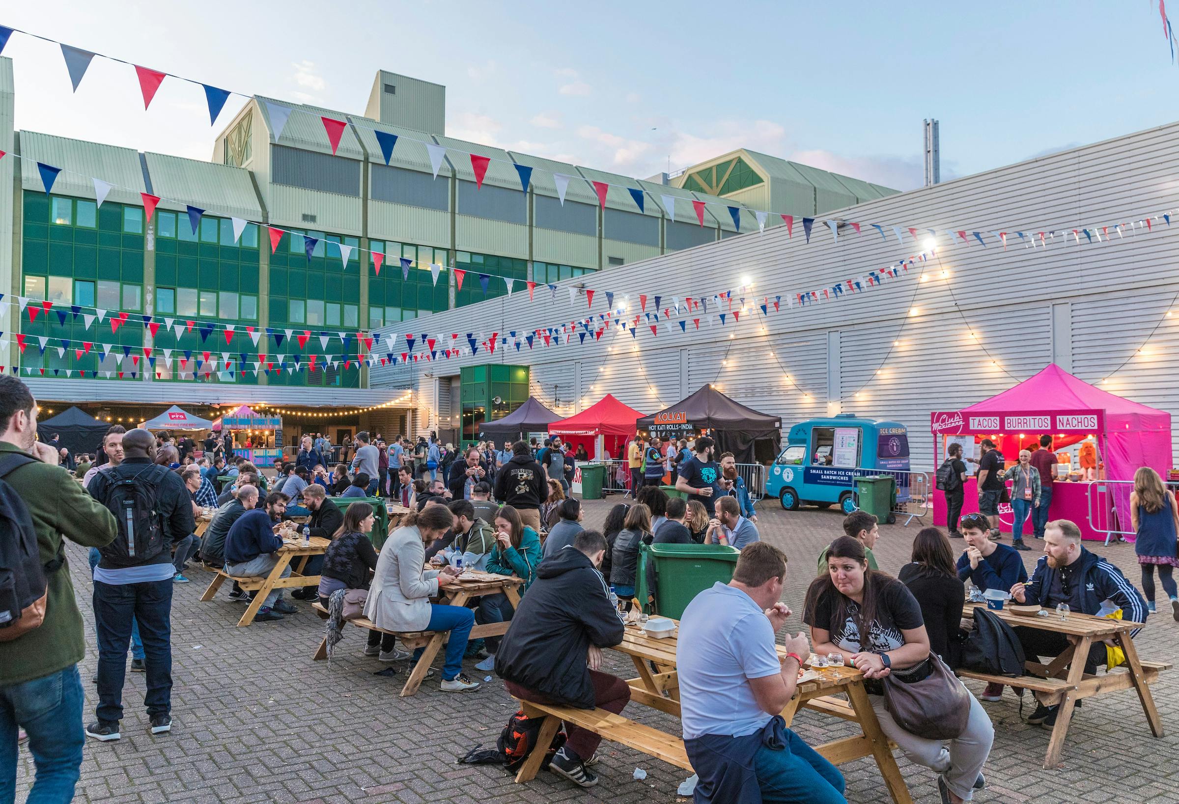 Vibrant outdoor event space in Printworks London with communal tables and food stalls.