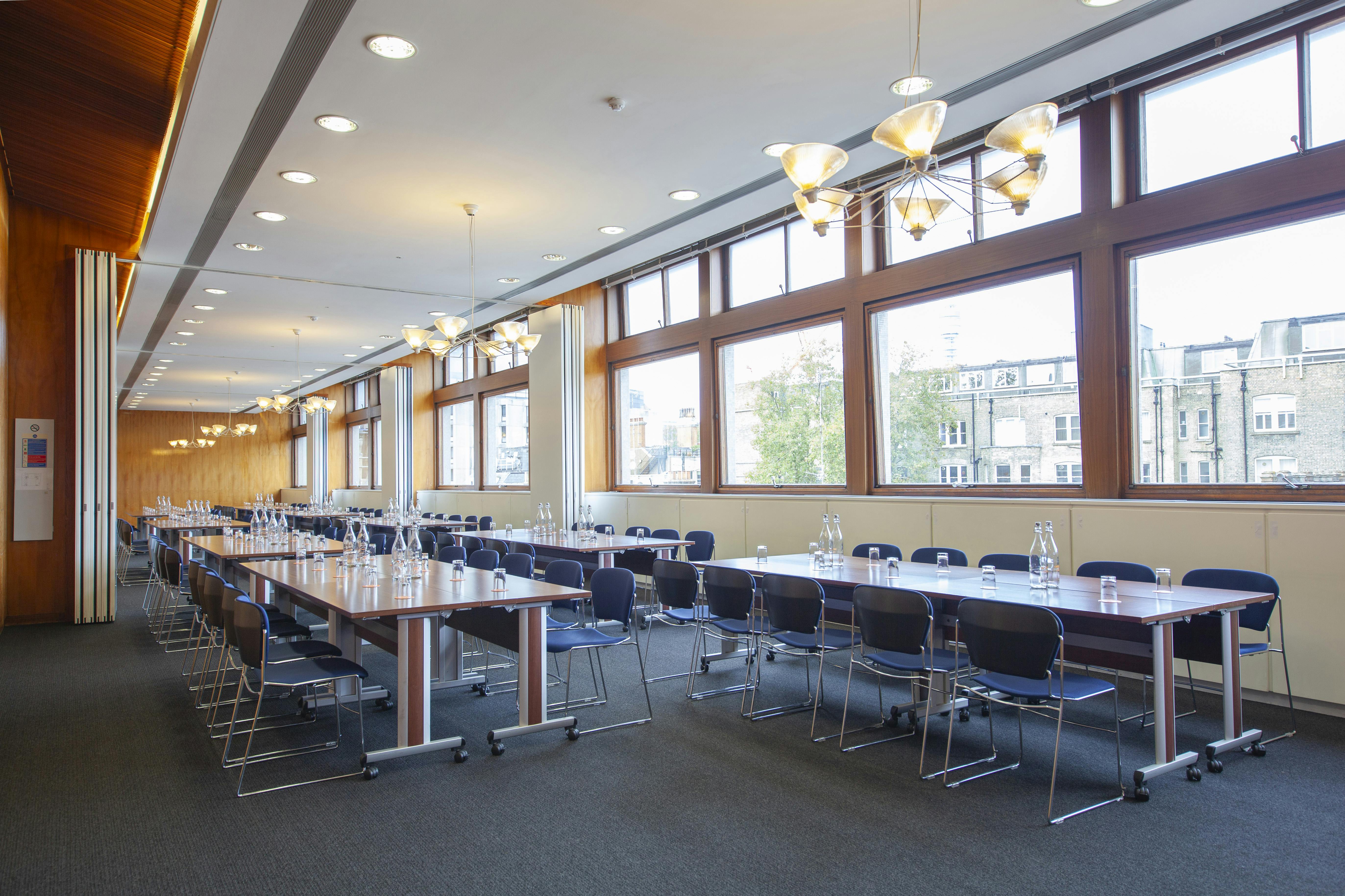 Well-lit flexible meeting room with long tables for corporate workshops and events.