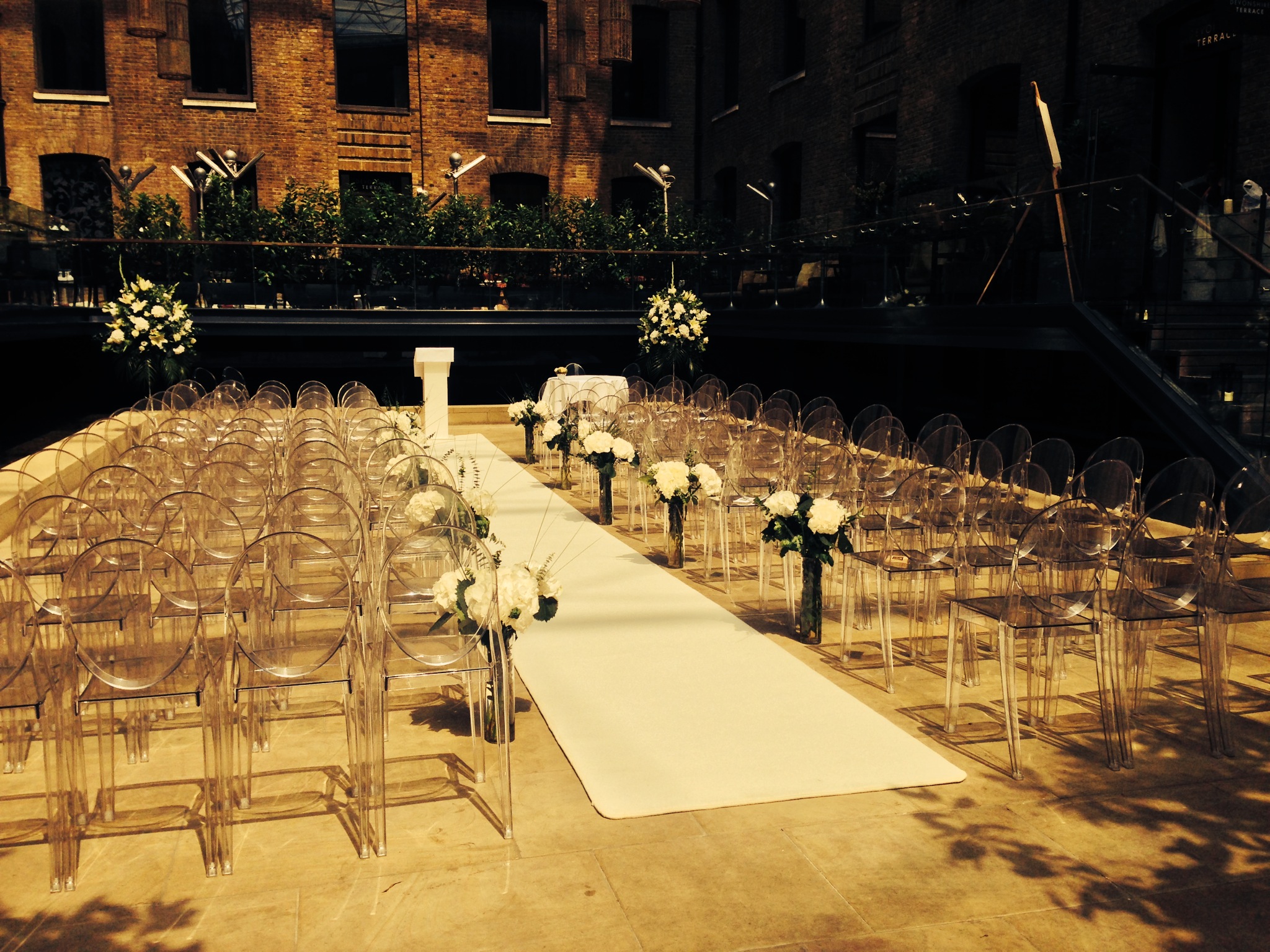 Outdoor wedding ceremony setup at Devonshire Terrace with elegant acrylic chairs and floral decor.
