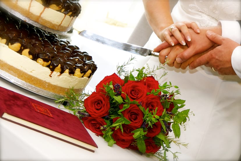Bournville Suite wedding scene with couple's hands, red roses, and elegant cake.