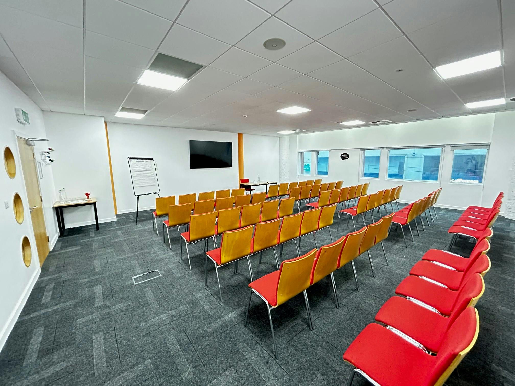 Meeting room with red chairs and large screen for workshops in Birmingham.