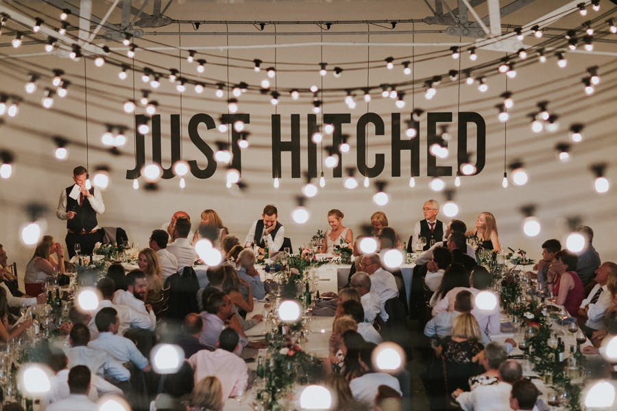 Wedding reception at Shoreditch Studios with "JUST HITCHED" backdrop and string lights.