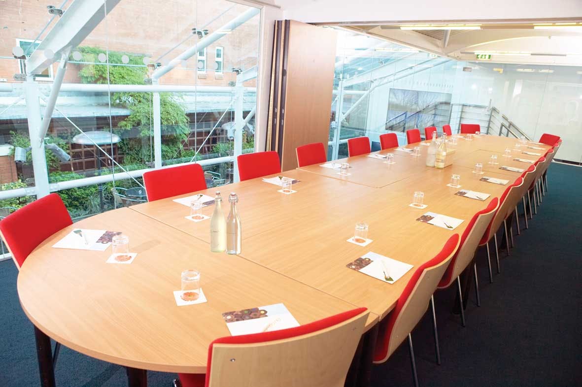 Meeting room with oval table and red chairs, perfect for corporate workshops.