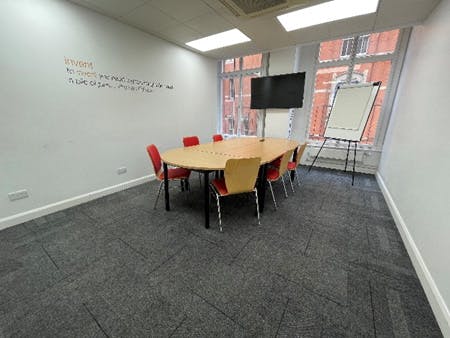 Well-lit meeting room with round table and red chairs, perfect for brainstorming sessions.